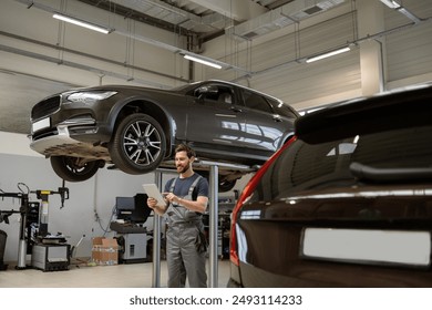 Mechanic in garage using tablet while inspecting elevated SUV. Workshop setting with cars, tools, and equipment. Concept of automotive repair, technology, and maintenance.
