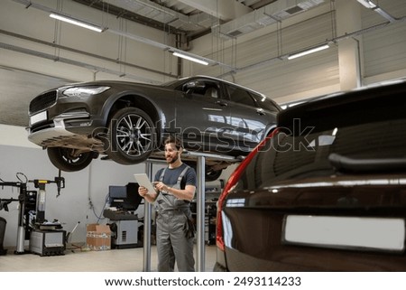 Mechanic in garage using tablet while inspecting elevated SUV. Workshop setting with cars, tools, and equipment. Concept of automotive repair, technology, and maintenance.