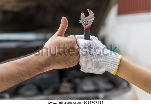 Mechanic hand checking and fixing
a broken car in  garage.hand of mechanic with thumbs up and
tool