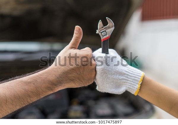 Mechanic hand checking and fixing\
a broken car in  garage.hand of mechanic with thumbs up and\
tool