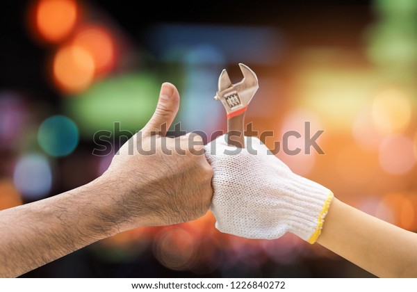 Mechanic hand\
checking and fixing a broken car in  garage.hand of mechanic with\
thumbs up and tool,bokeh\
background