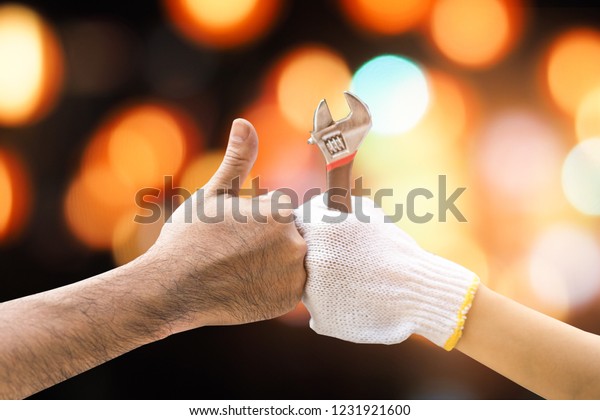 Mechanic hand\
checking and fixing a broken car in  garage.hand of mechanic with\
thumbs up and tool,bokeh\
background