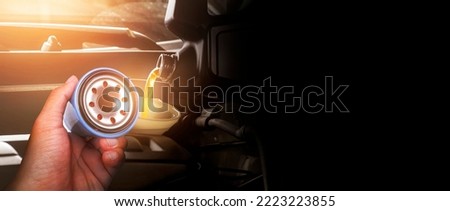 Mechanic hand showing oil filter against the background pouring motor oil into the car engine in the engine compartment ,  panoramic banner with copy space on black background.