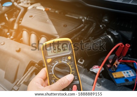 Mechanic hand use multimeter voltmeter to check the voltage level in a car battery.
