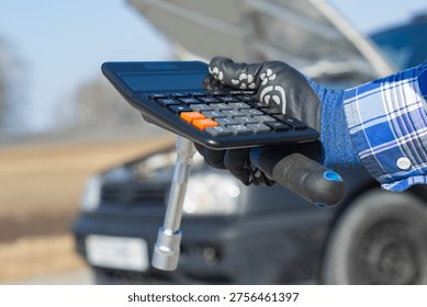 Mechanic hand using calculator while holding wrench near car, representing vehicle repair cost estimation and service pricing. Automotive maintenance, budgeting and financial planning