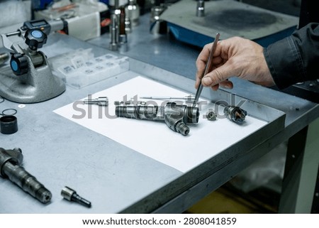 Mechanic hand using tweezers for small internal part installation during diesel fuel injector repair in workshop