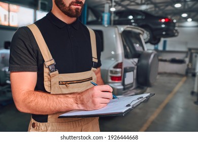 A mechanic holding a clipboard in the auto repair shop. Car checking and repairing concept. Cropped image.