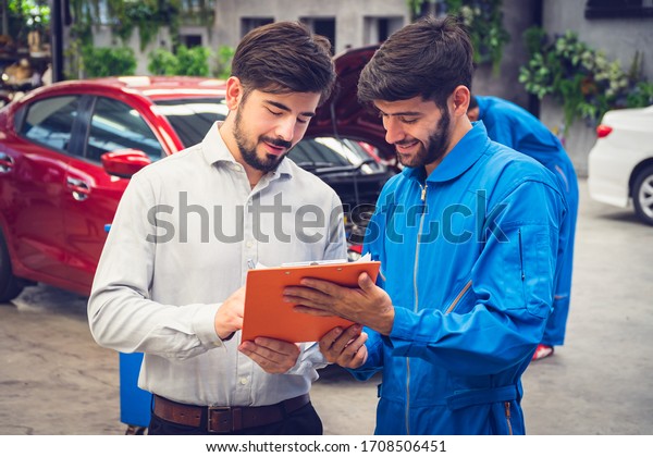 Mechanic holding clipboard with car\
owner in the workshop garage. Car auto services\
concepts
