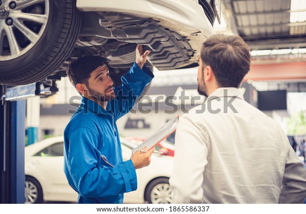 Mechanic holding clipboard with car
owner in the workshop garage. Car auto services
concepts