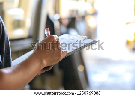 Mechanic holding clipboard with checking truck in service center,
Preforming a pre-trip inspection on a truck,preventive maintenance,spot focus
