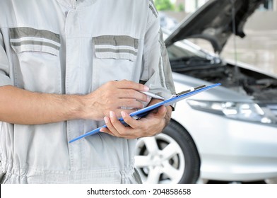 A mechanic holding clipboard in front of car engine - car checking & repairing concept