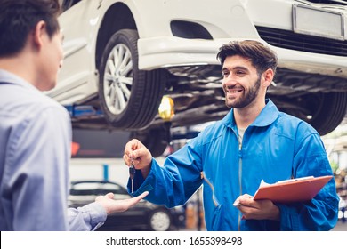 Mechanic Holding Clipboard Giving The Key Back To Car Owner In The Workshop Garage. Car Auto Services Concepts