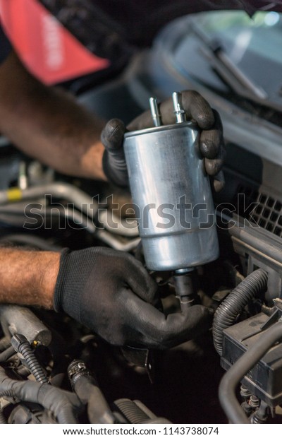Mechanic holding a fuel filter over\
the car hood, auto repairing or servicing concept\

