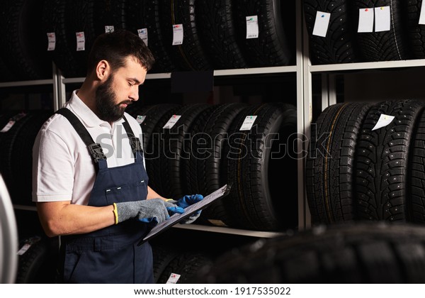 Mechanic holding paper tablet document in hands\
while checking the assortment in car repair service, expertise\
mechanic working in automobile repair garage alone, serve the\
customers