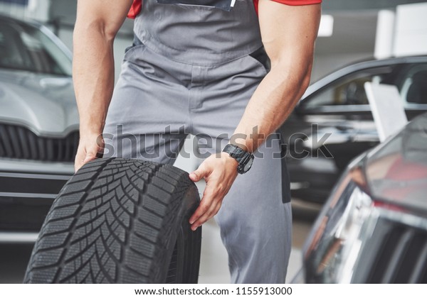 Mechanic holding a tire tire at the repair\
garage. replacement of winter and summer\
tires.