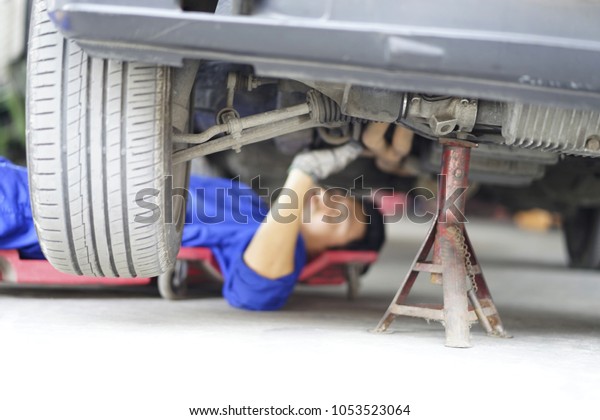The mechanic\
holding wrench in hand for fix car. Strong Man fix under the car in\
garage with wrench. Mechanic lying down and working under the front\
of automobile in store. 