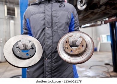 The mechanic holds old rusty brake disc and new disc. Change the old to new brake disc on car in a garage. Auto repair concept. - Shutterstock ID 2256662179