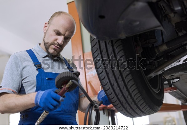 Mechanic inflating a tire and\
checking air pressure with a pressure gauge at the auto repair\
shop