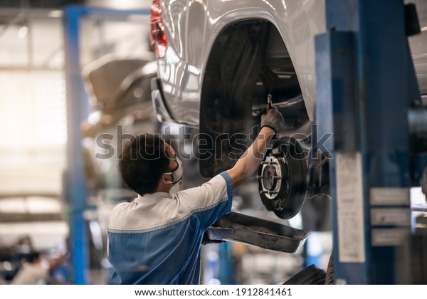 Mechanic inspecting car suspension detail\
and wheel car of lifted automobile at repair service station. Car\
service station. Preventive\
maintenance.