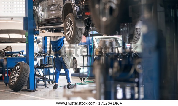 Mechanic inspecting car suspension detail\
and wheel car of lifted automobile at repair service station. Car\
service station. Preventive\
maintenance.