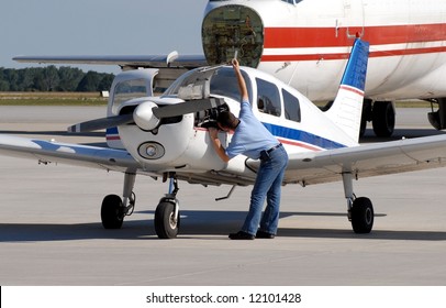 Mechanic Inspecting A Small Engine Aircraft, Larger Airplane In Background