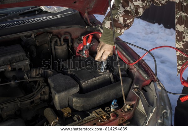 Mechanic jumper cables\
connected to a discharged battery.\
Firing the car in the winter by\
the jumper cables.