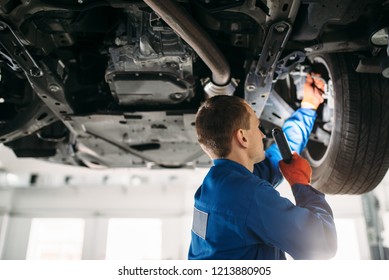 Mechanic with lamp checks car brake hoses