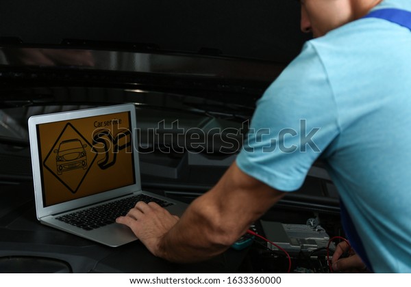 Mechanic with laptop doing car diagnostic at\
automobile repair shop,\
closeup