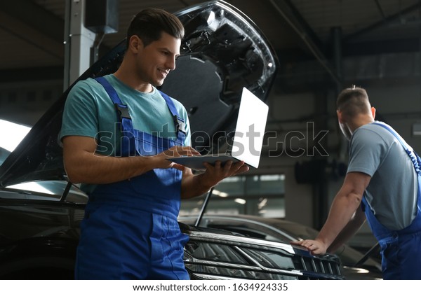 Mechanic with laptop doing car diagnostic at\
automobile repair shop