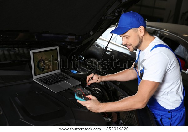 Mechanic with laptop doing car diagnostic at\
automobile repair shop