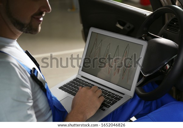 Mechanic with laptop doing car diagnostic at\
automobile repair shop,\
closeup