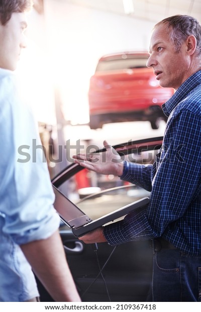 Mechanic with laptop talking to customer in auto\
repair shop