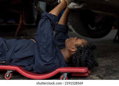 Mechanic lying down and working under car at auto service garage. Technician vehicle maintenance and checking under car at automotive motor garage.