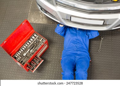 Mechanic lying and working under car at the repair garage - Powered by Shutterstock