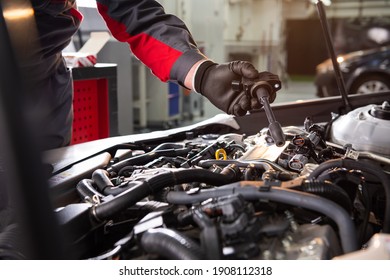 mechanic makes diagnostics of the car in the engine. car service and audit by an employee in a large car service. candle replacement. black mittens and car tool 