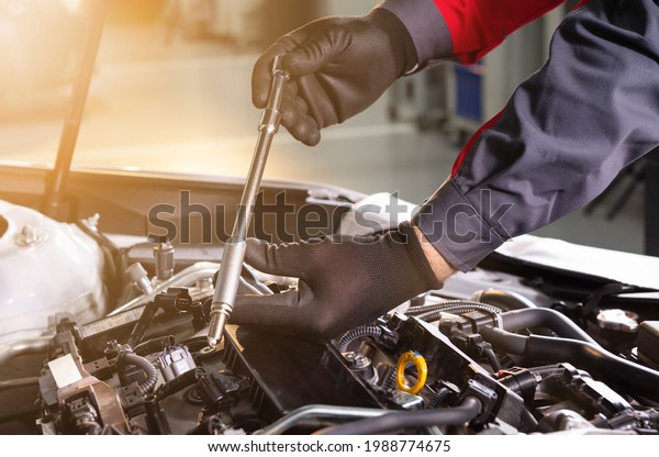 mechanic makes diagnostics of the\
car in the engine. car service and audit by an employee in a large\
car service. candle replacement. black mittens and car tool\
