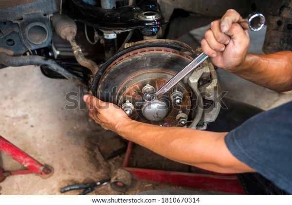 Mechanic man close up fixing repairing car rotor\
spindle hub automobile vehicle parts examining using tools\
equipment working hard in workshop garage support and Replace brake\
disc and pads