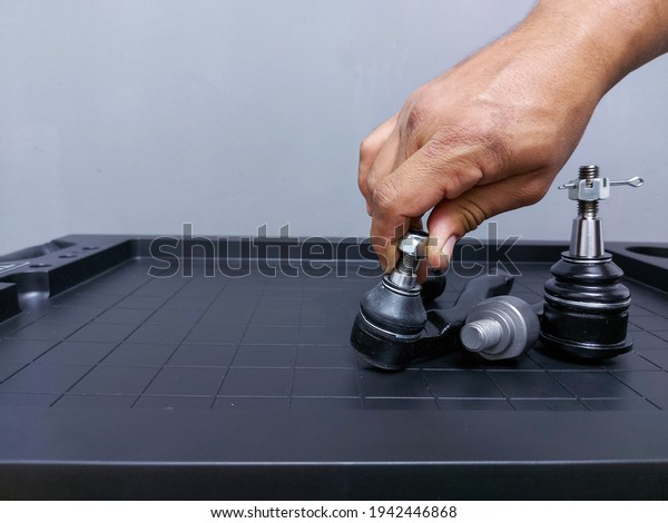 mechanic man hand placing a lock nut to a\
steering terminal on a table with spare parts in front of car or\
truck on gray background and space for\
copy