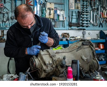 Mechaniker in seiner Werkstatt mit blauem Anzug inspizieren Getriebe eines Autos, das er auf einem Tisch hat