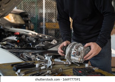 Mechanic man holding alternator of the car on working table in repair and maintenance garage 