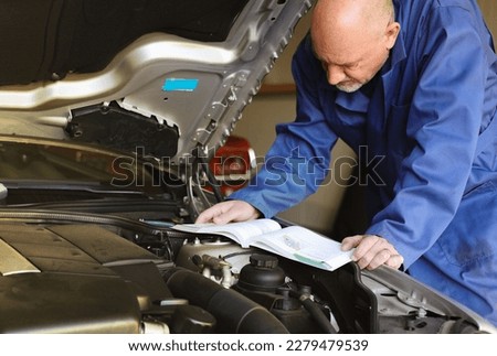 Mechanic man holding and reading the car user manual or user instruction to checking or fixing engine of modern car in garage. Car maintenance or service before driving concept.