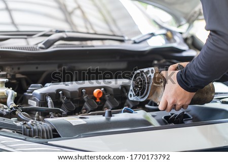 Mechanic man holding starter motor of the car on working table in repair and maintenance garage 