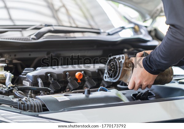 Mechanic man holding starter motor of\
the car on working table in repair and maintenance garage\
