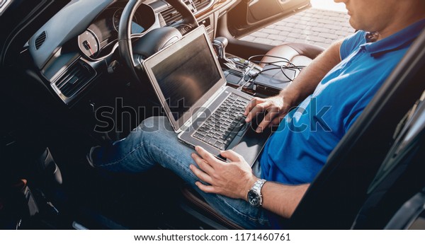Mechanic man with laptop making car\
diagnostics at auto service.\
Background