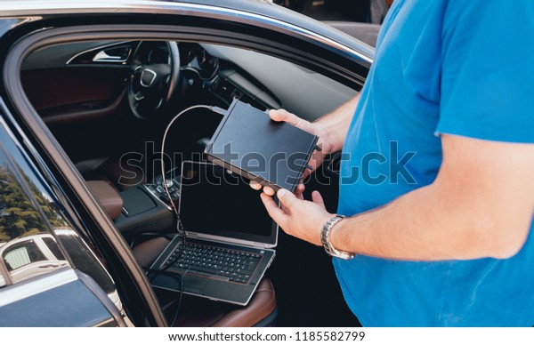 Mechanic man with laptop making car\
diagnostics at auto service.\
Background