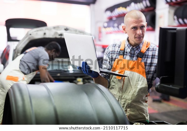 Mechanic man with laptop making car diagnostics\
at auto service
