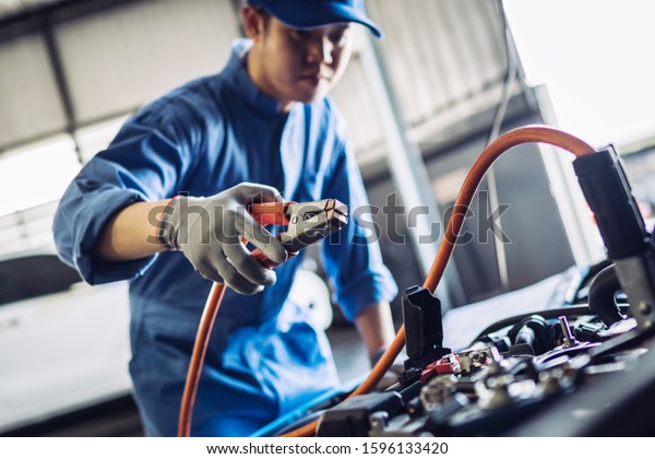 Mechanic man maintenance jump battery charging the\
engine a vehicle car hood, Safety inspection test engine before\
customer drive on a long journey, transportation repair garage\
service center