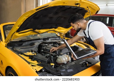 Mechanic man mechanic manager worker using a laptop computer checking car in workshop at auto car repair service center. Engineer young man looking at inspection vehicle details under car hood - Shutterstock ID 2220681903