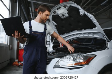 Mechanic man mechanic manager worker using a laptop computer checking car in workshop at auto car repair service center. Engineer young man looking at inspection vehicle details under car hood. - Powered by Shutterstock