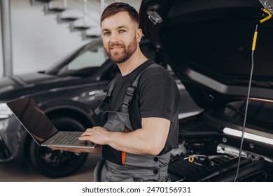 Mechanic man mechanic manager worker using a laptop computer checking car in workshop at auto car repair service center. Engineer young man looking at inspection vehicle details under car hood. - Powered by Shutterstock